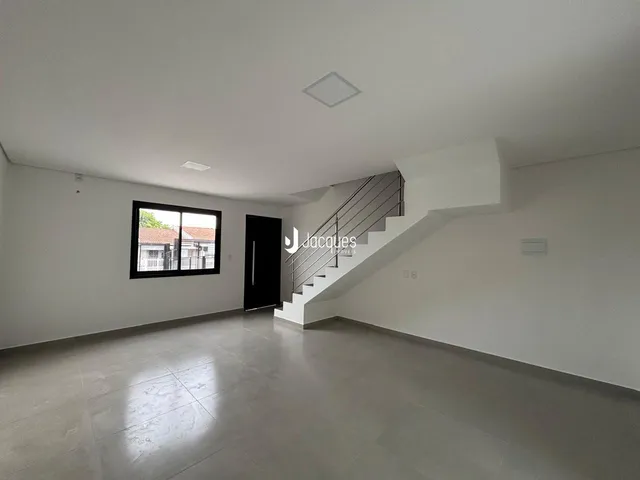 Esta é uma sala de estar ampla com piso claro e uma escadaria.