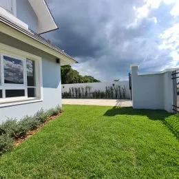 Vista externa de um jardim gramado com uma parede branca de uma residência em Lajeado.