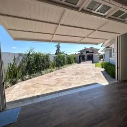 Área externa pavimentada com piso de pedra e vegetação ao fundo.