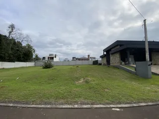 Vista externa de um terreno com gramado verde e construções ao fundo.