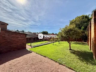Vista externa de um jardim gramado com árvores e muros de tijolos.
