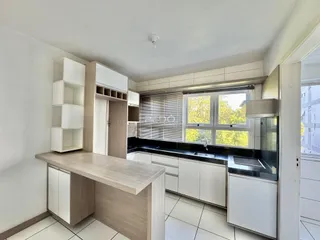 Cozinha moderna com armários brancos e bancada escura em um apartamento no Brasil.