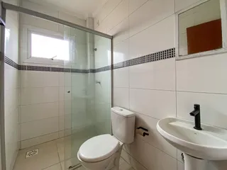 Foto de um banheiro com box de vidro, vaso sanitário e pia brancos.