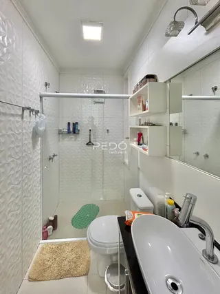 Foto interna de um banheiro com revestimento cerâmico e box de vidro.