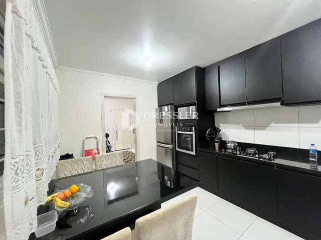 A cozinha com armários escuros e bancada escura é visível na imagem.