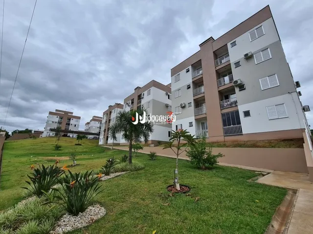 Gramado verde com vegetação na frente de um edifício residencial.