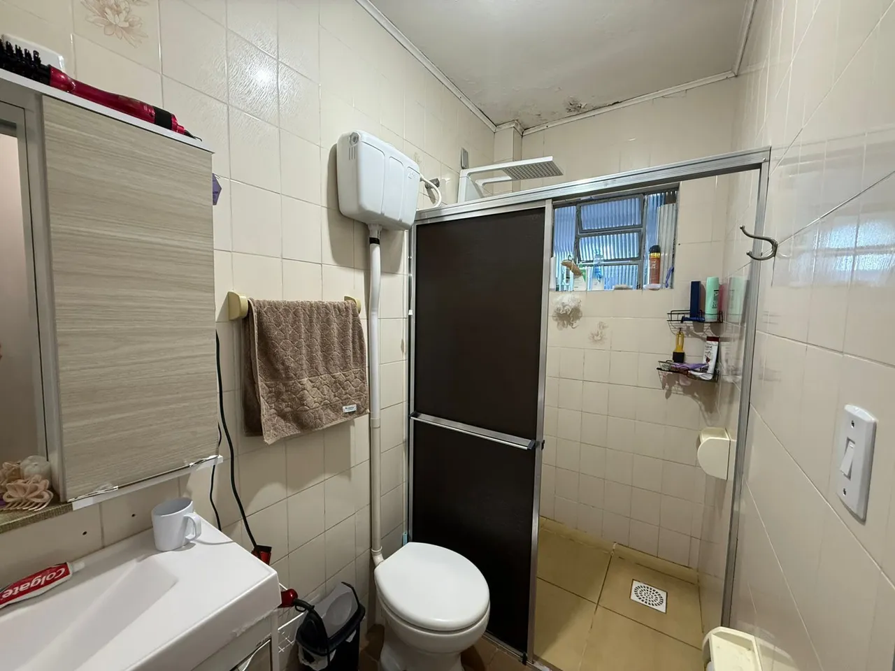 Banheiro com revestimento de azulejos brancos e box de vidro.