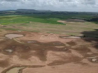 Vista aérea de uma área rural com campos abertos e vegetação sob um céu nublado.