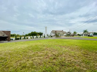 Vista externa de uma propriedade com gramado em primeiro plano e casas ao fundo.