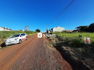Vista de uma estrada de terra em uma área rural com construções ao fundo sob um céu azul claro.