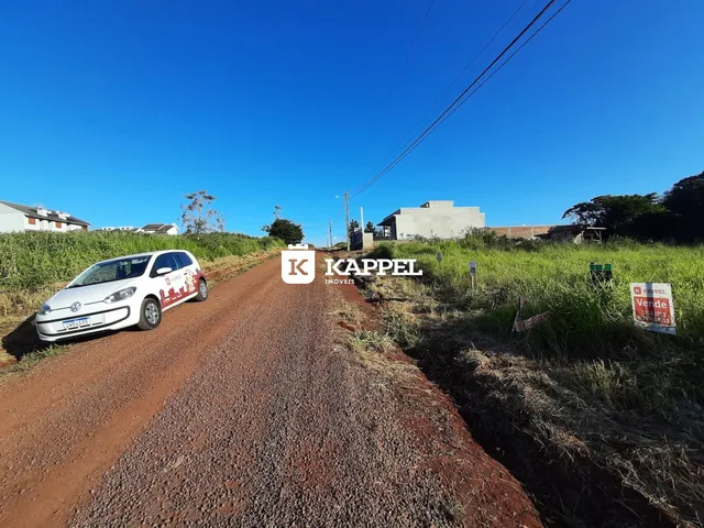 Vista de uma estrada de terra em uma área rural com construções ao fundo sob um céu azul claro.