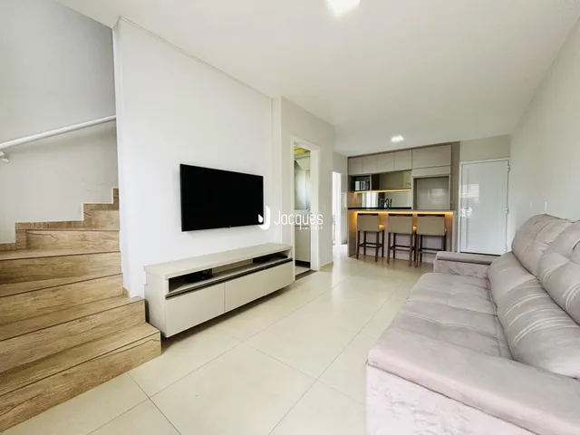 Sala de estar com cozinha integrada e escadaria de madeira.