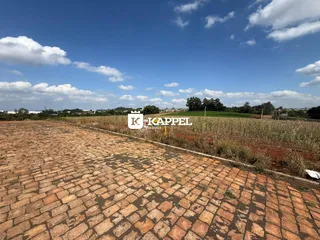 Vista externa mostrando um pátio pavimentado e uma área de campo aberto sob um céu azul.