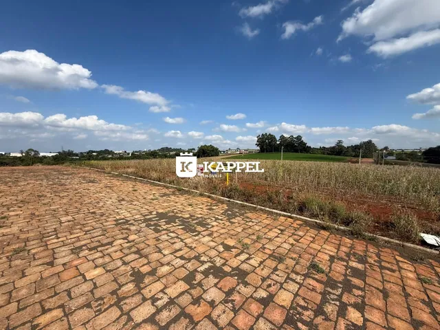 Vista externa mostrando um pátio pavimentado e uma área de campo aberto sob um céu azul.