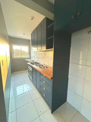 Vista interna de uma cozinha moderna com armários escuros e piso claro.