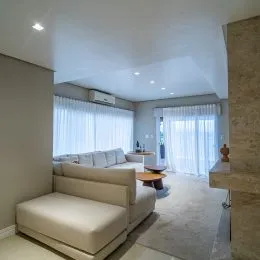 Sala de estar com grandes janelas cobertas por cortinas brancas.