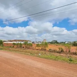 Uma estrada de terra vermelha com vegetação rasteira em um campo aberto.