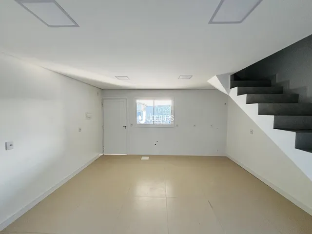 Interior de uma sala ampla com paredes brancas e piso claro.