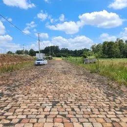Vista de uma estrada de terra que se estende por um campo aberto sob um céu azul.