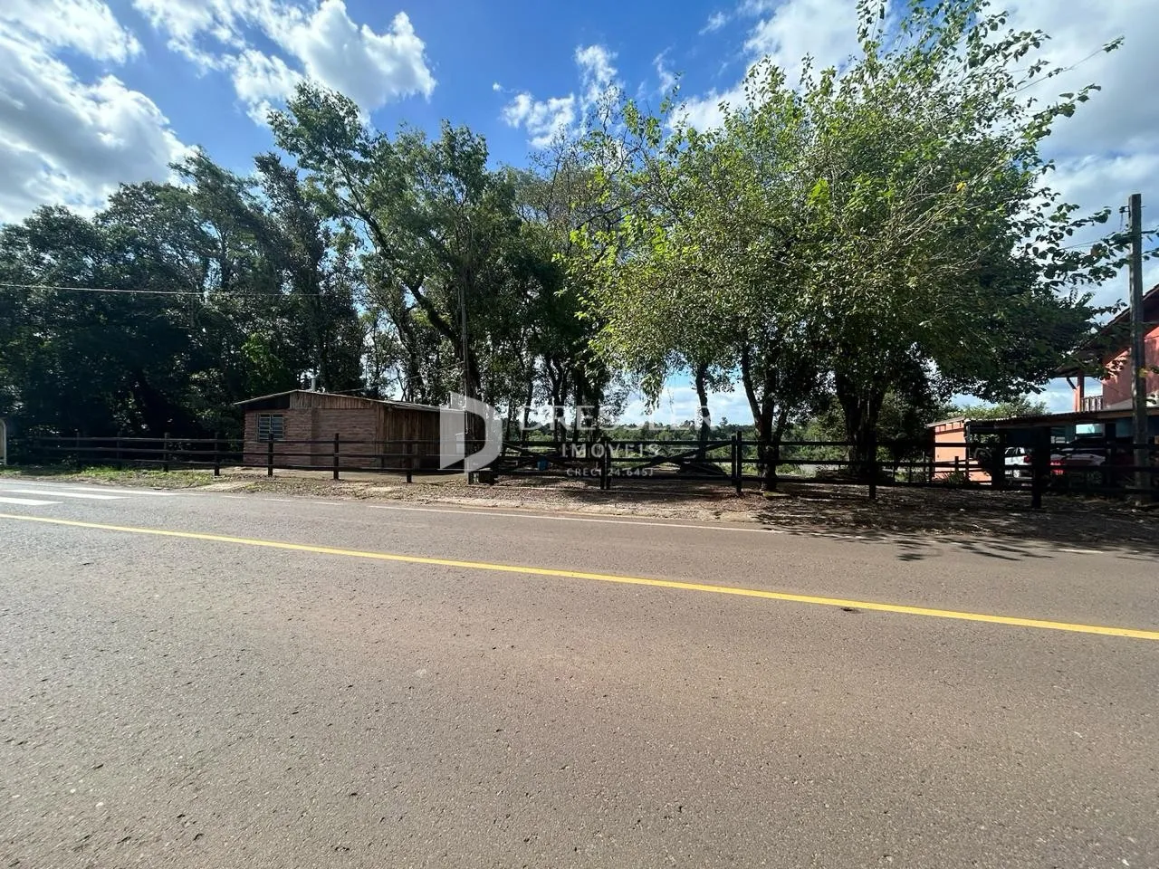 Vista da propriedade ao longo de uma estrada com vegetação e cerca.