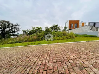 Vista externa de uma propriedade com jardim e pavimentação de paralelepípedos.