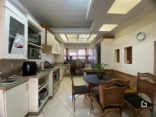 Ambiente de cozinha e jantar com armários brancos e mesa de madeira no imóvel.