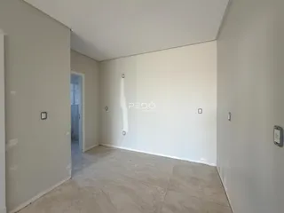 Vista interna de um corredor com paredes brancas e piso de concreto claro.