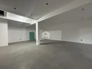 Imagem de um espaço interno vazio com paredes brancas e piso cru.