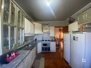 Vista interna de uma cozinha com armários brancos e piso de madeira.