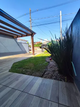 Vista externa de um jardim com deck de madeira e vegetação.