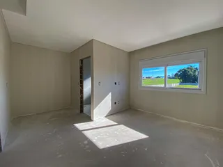 Uma sala vazia com paredes claras e uma grande janela mostrando a paisagem externa.