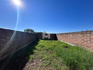 Vista de um terreno delimitado por muros de tijolos e vegetação.