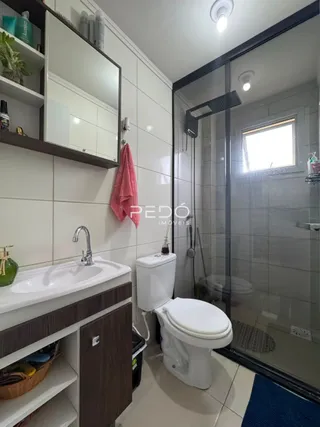 Banheiro com box de vidro e louças brancas.