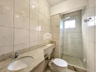 Interior de um banheiro com revestimento cerâmico e box de vidro.