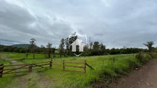 Vista de um campo gramado com cerca de madeira e vegetação ao fundo.