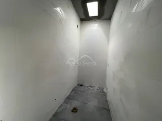 Corredor interno com paredes brancas e piso de concreto aparente.
