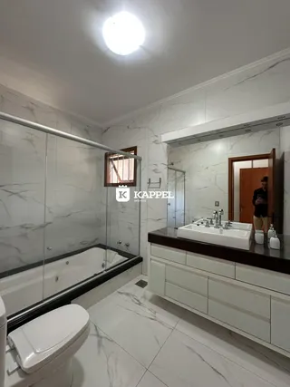 Banheiro com revestimento em mármore e box de vidro.