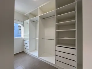 Vista interna de um corredor com estantes e armários brancos.