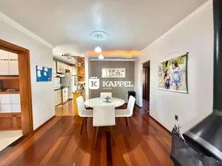 Vista de uma sala de jantar com mesa branca e cadeiras em um ambiente com piso de madeira.