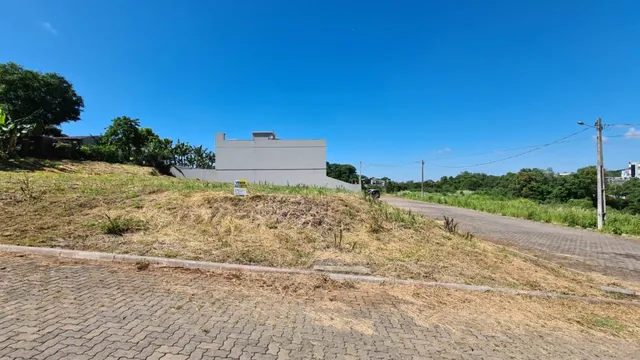 Vista externa de uma área gramada com estrada de terra sob um céu azul.