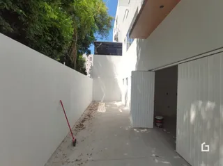 Vista da fachada de um prédio branco com vegetação ao redor.