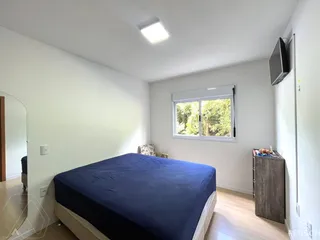 Quarto com cama azul e janela com vista para a vegetação externa.