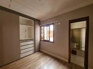 Vista interna de um corredor com piso de madeira clara e porta de entrada para um banheiro.