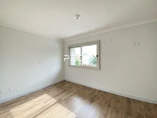 Vista interna de uma sala com piso de madeira clara e paredes brancas.