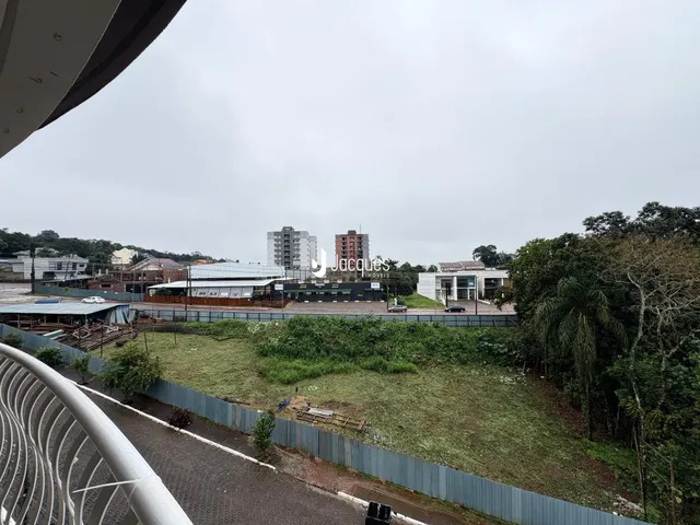 Vista externa de uma propriedade com vegetação e estruturas ao fundo.