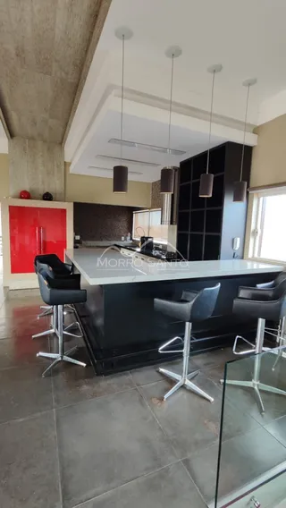 Foto de uma cozinha moderna com ilha escura e banquetas em um ambiente com teto de concreto aparente.