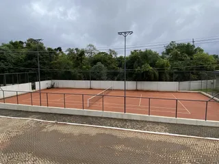 Foto de uma quadra esportiva externa com piso avermelhado e cerca.
