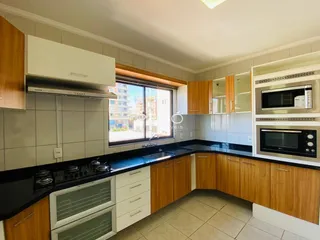 Vista da cozinha moderna com armários de madeira e bancadas escuras.