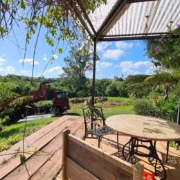 Deck de madeira com mesa e cadeiras em uma área externa com vegetação.
