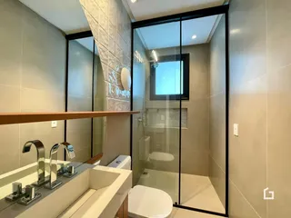 Banheiro com bancada dupla e box de vidro transparente.